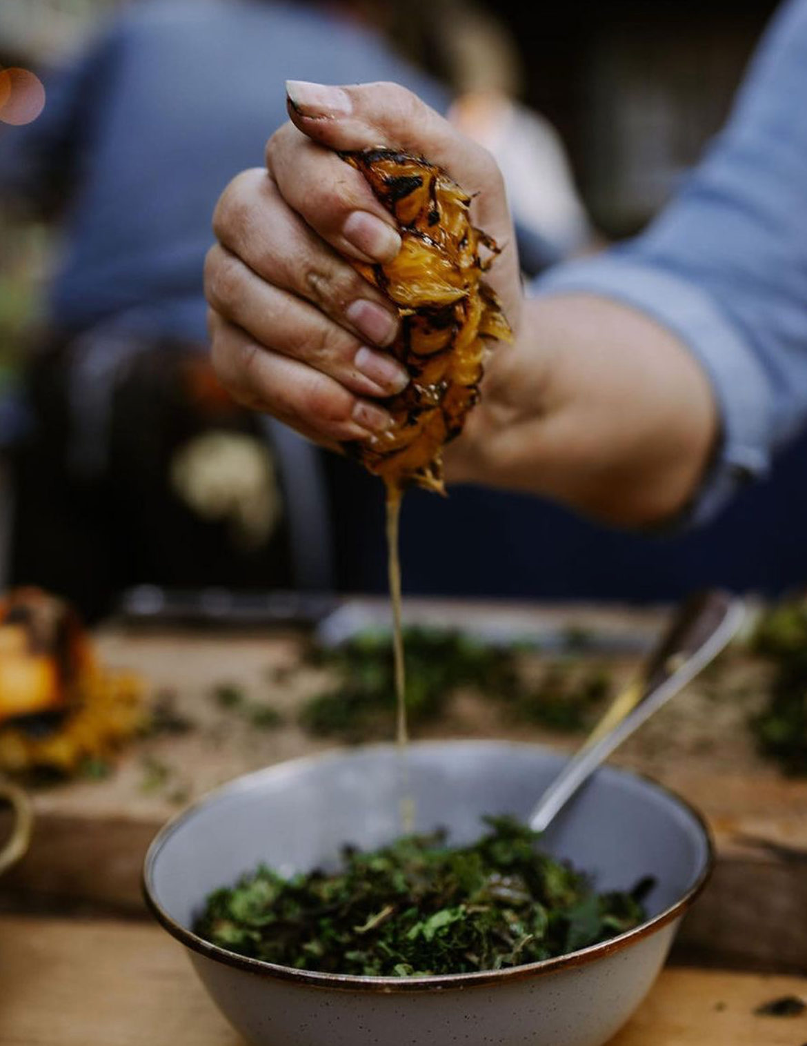 A hand squeezing roasted wild fruit over greens